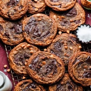 Thin, chewy, and ripple-edged butterscotch chocolate chip cookies on a cooling rack, on a burgundy backdrop.